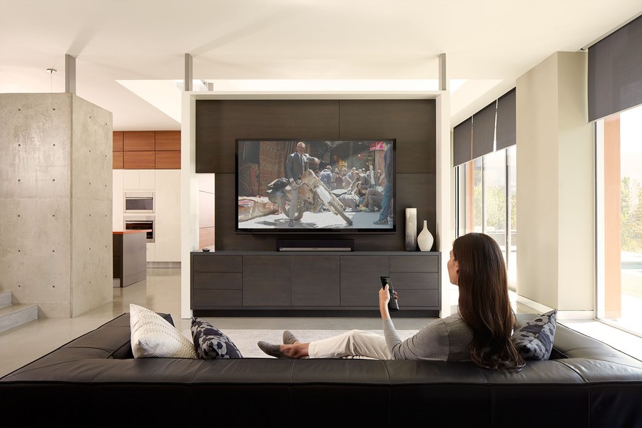 A woman is watching TV and controlling her content with a Savant remote.