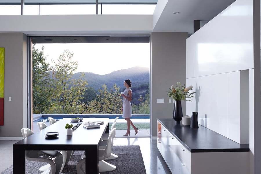 A woman in a luxury, modern home looks out her window to a forest.