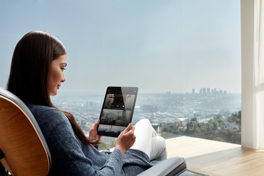A woman sitting in a chair with a view overlooking a city and holding an iPad displaying the Savant app.