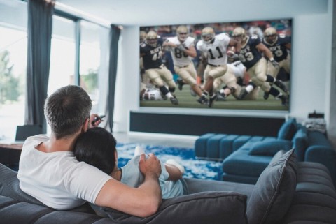 A couple in a media room enjoying a football game on the screen.