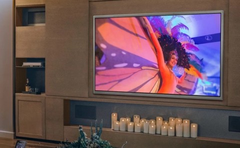 Large screen TV mounted on the wall with several lit candles beneath it and in-wall speakers 