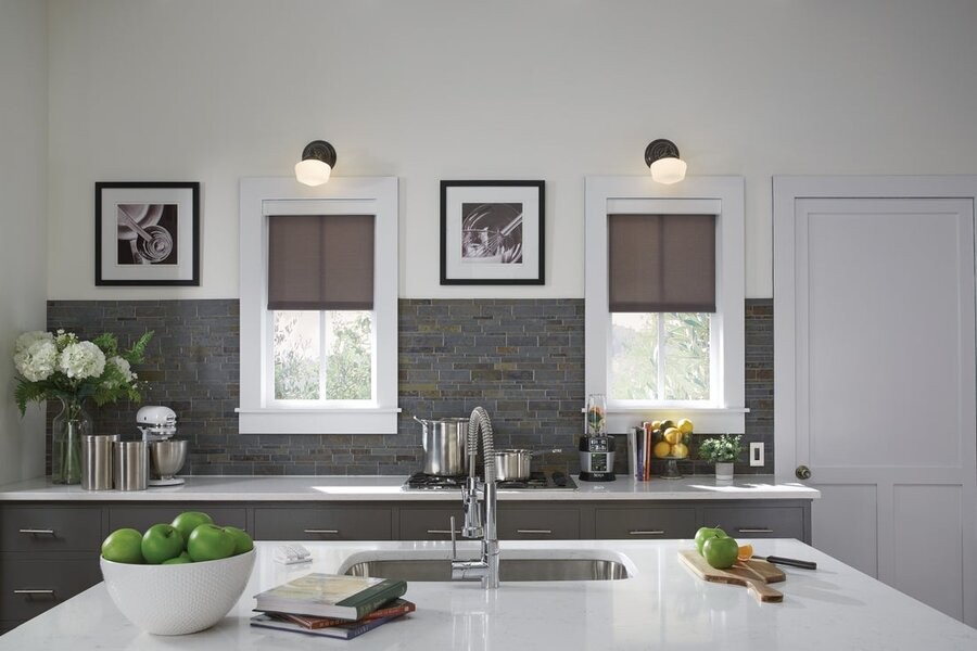 A kitchen space featuring two windows with a Lutron lighting fixture above each and two Lutron motorized shades lowered halfway.