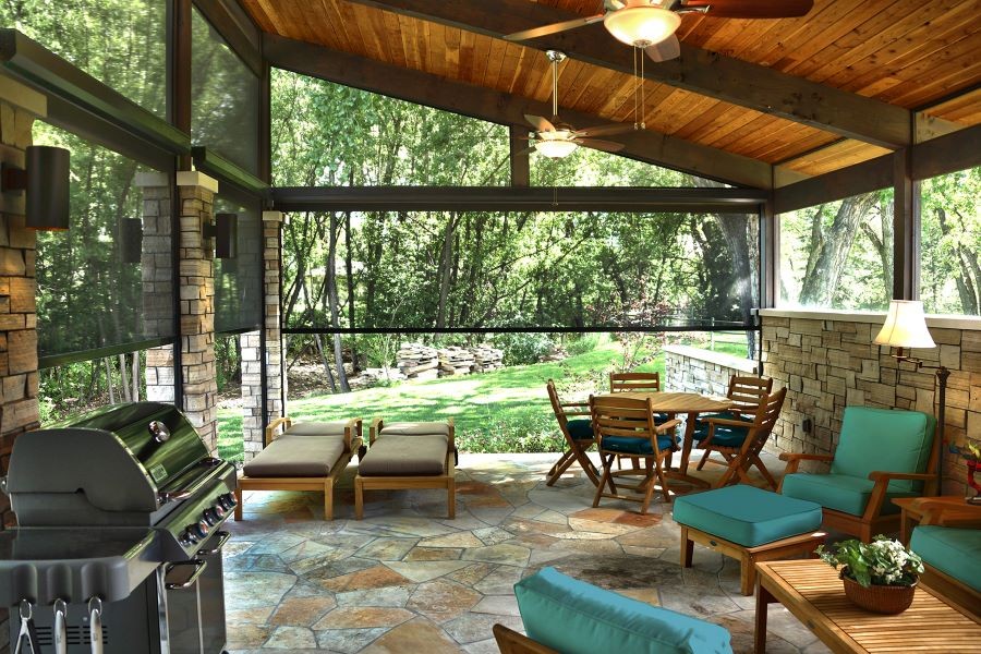 Outdoor motorized shades partially lowered around a patio area with furniture and a grill.