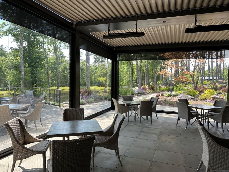 A modern enclosed patio with retractable solar shades, showcasing an outdoor dining area with rattan chairs and tables. 