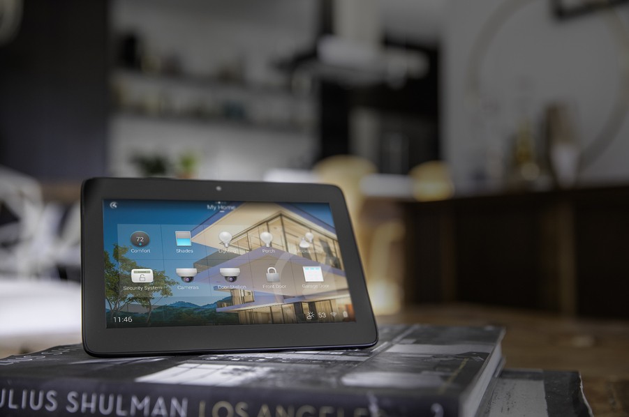 A close-up view of a tablet with a Control4 smart home automation interface, sitting on some coffee table books.