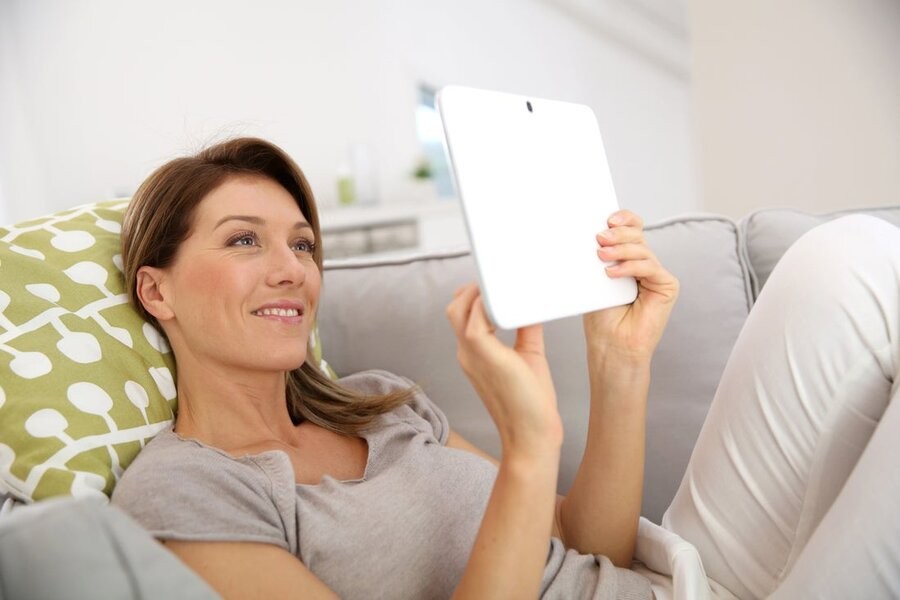 A woman sitting on her couch using a touchscreen tablet.