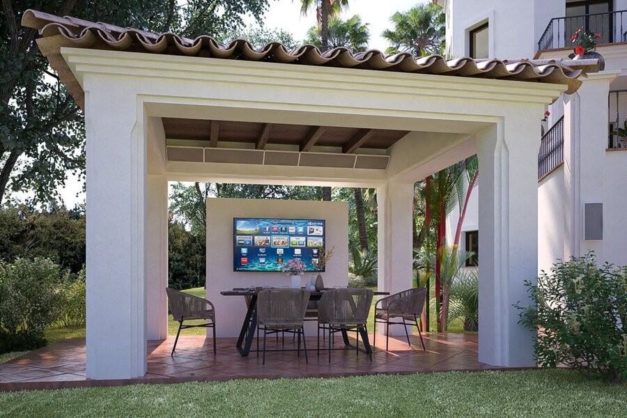 An outdoor entertainment setup in a backyard, featuring Coastal Source Razor outdoor speakers installed within a pergola.