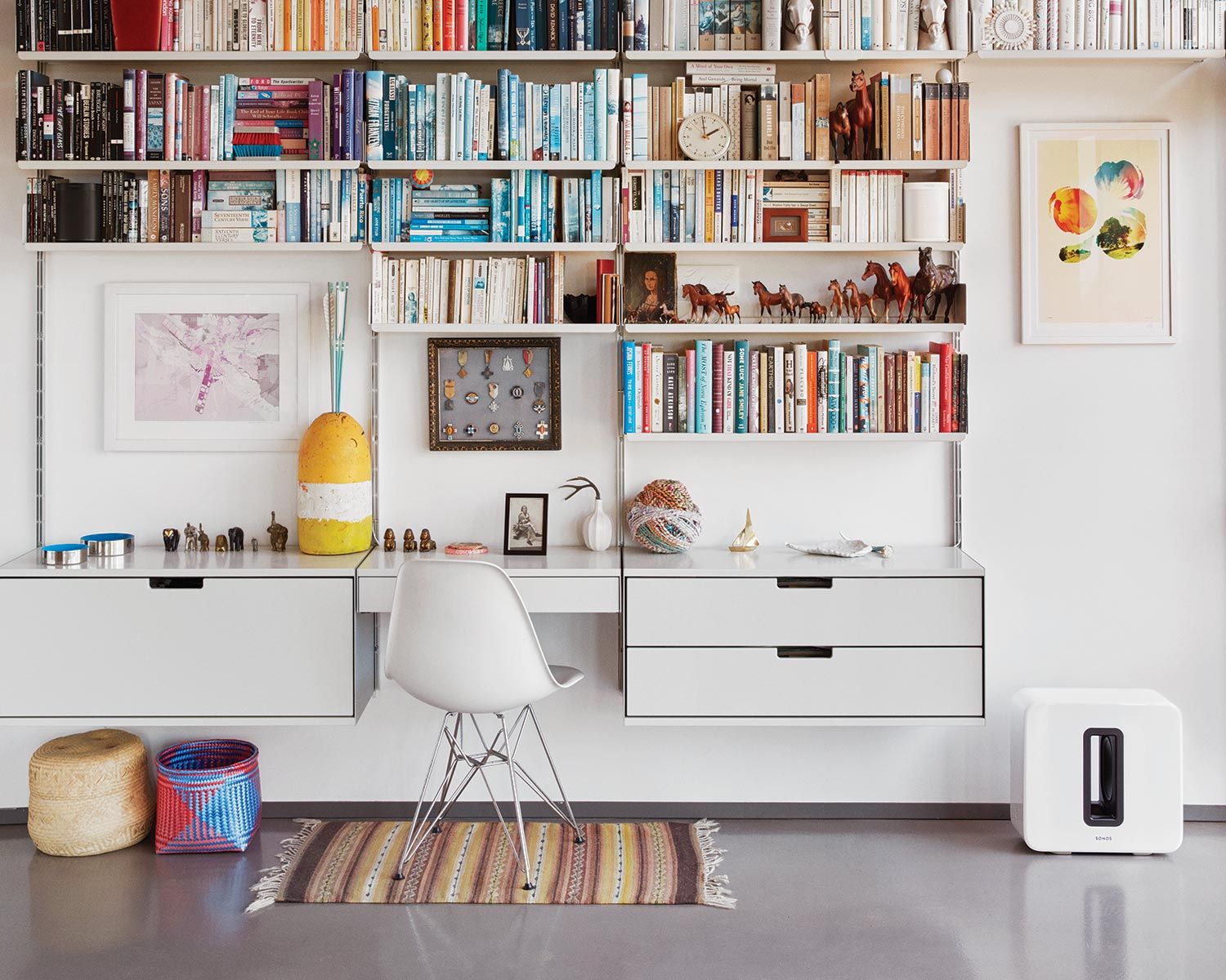 A modern home office with a bookshelf, a desk, and a white Sonos Sub speaker.