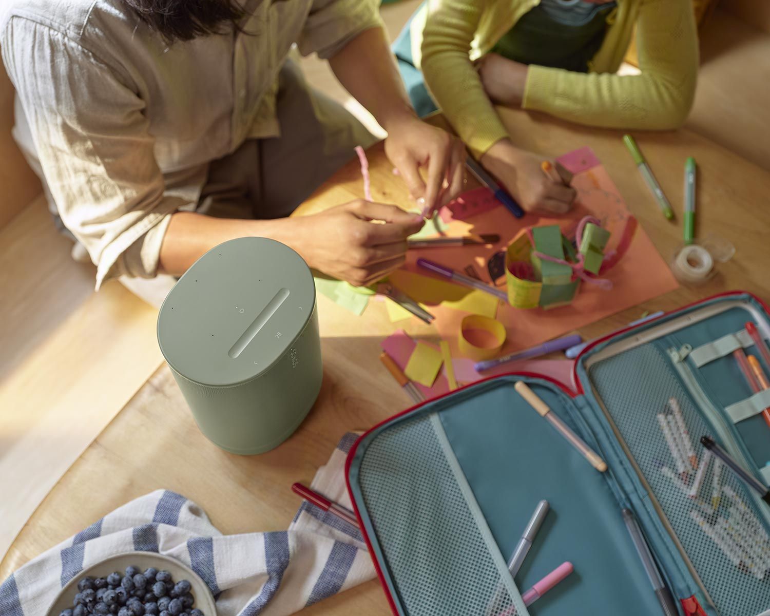 A person and a child doing arts and crafts on a table, with a green Sonos speaker nearby.