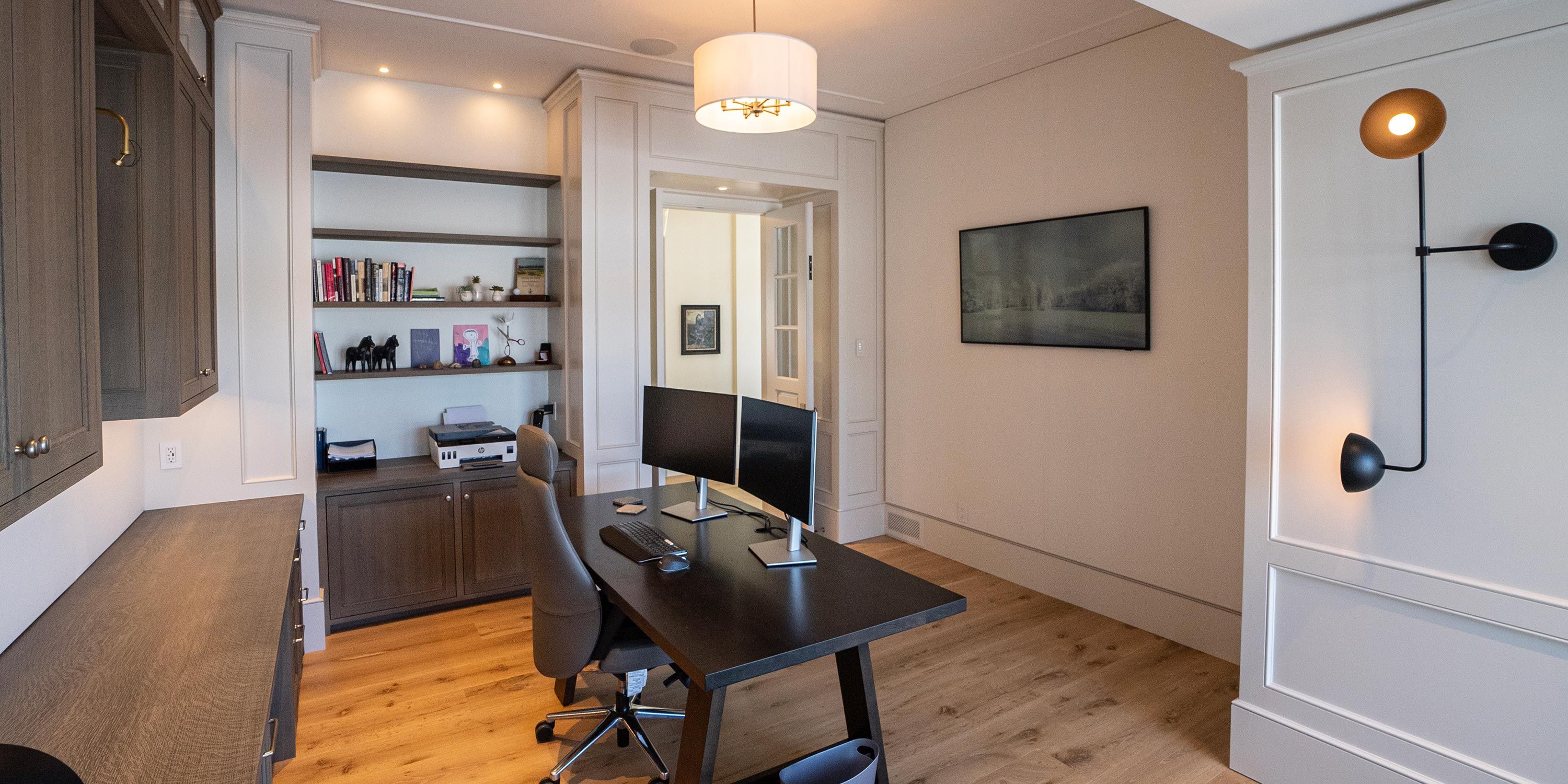 A well-organized home office featuring a large desk with dual monitors, built-in shelves, and soft ambient lighting.