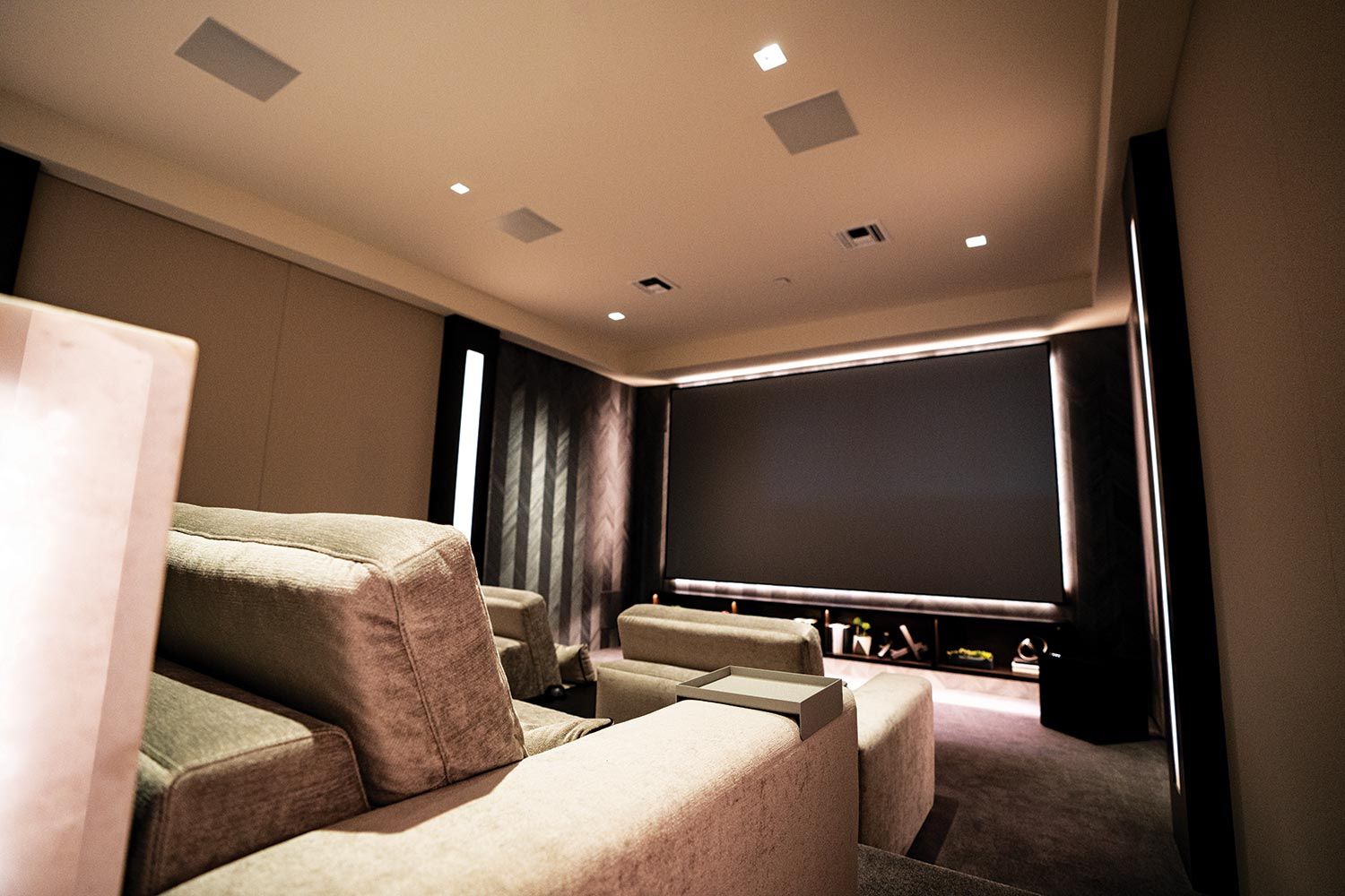 A compact yet stylish home theater with soft seating, recessed lighting, and a large projector screen set in a modern, dimly lit room.