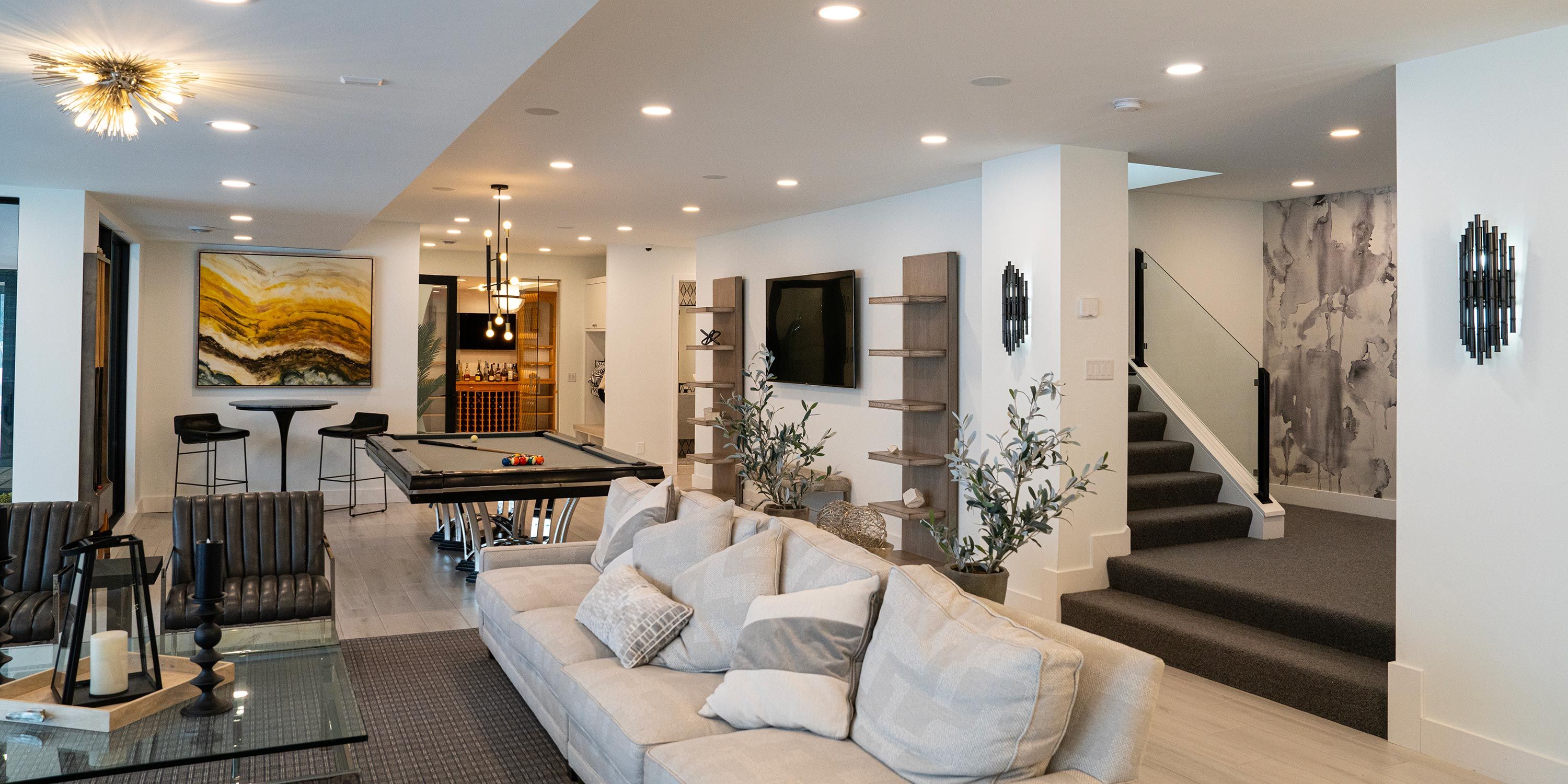 A stylish entertainment room with a large couch, pool table, and bar area, illuminated by modern light fixtures.