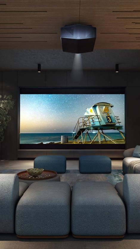 A modern Sony home theater with a large screen displaying a scenic image of a lifeguard tower at the beach under a starry sky. The room features plush seating and a ceiling-mounted projector.
