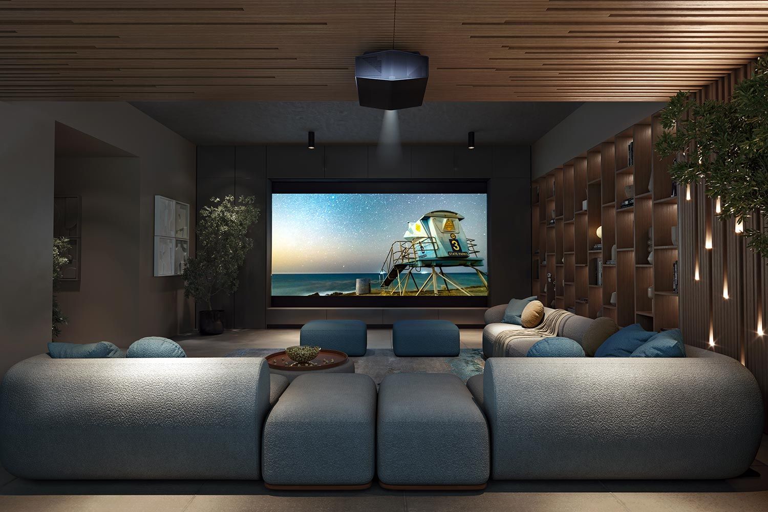 A spacious home theater with tiered seating, soft gray cushions, a large projector screen, and floor-to-ceiling windows overlooking a snowy landscape.