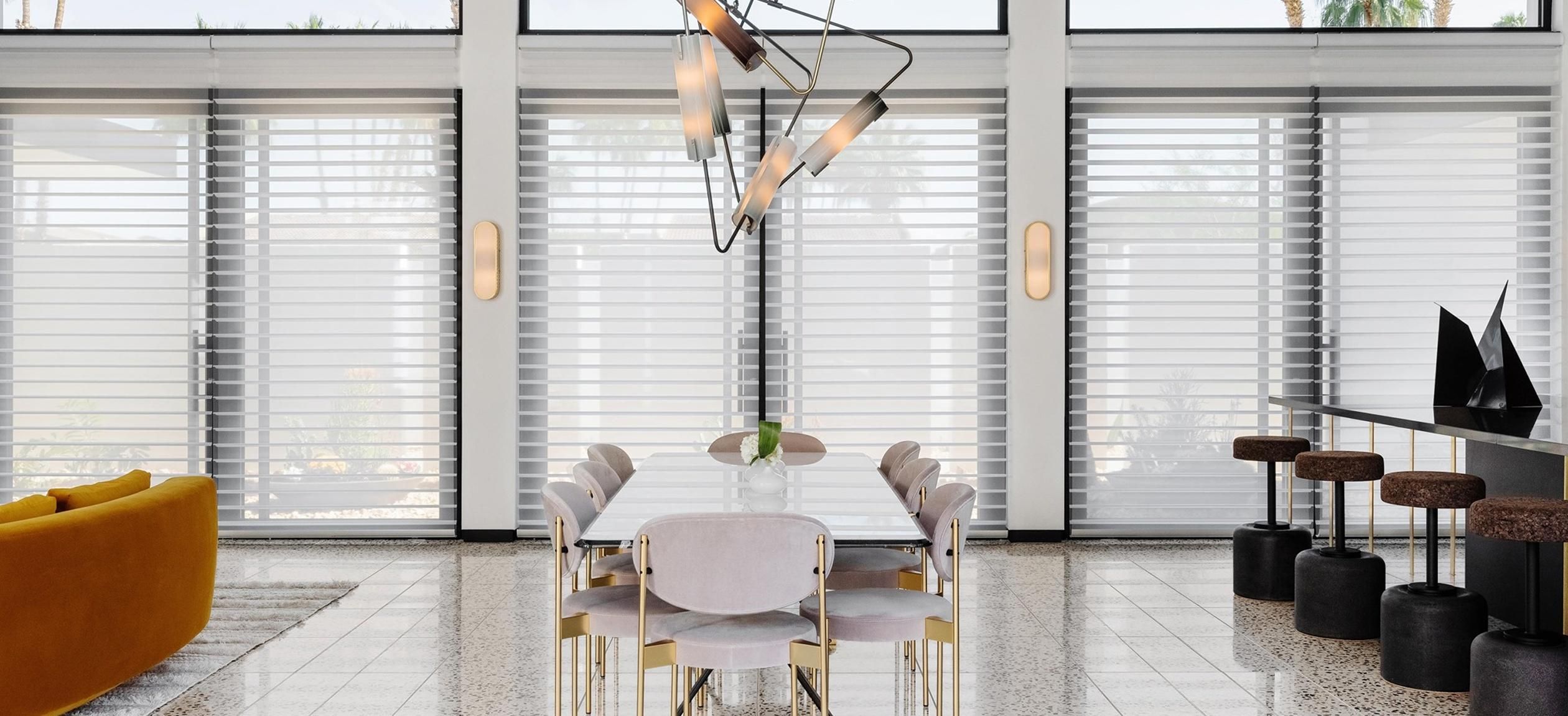 Modern dining area with large windows featuring Hunter Douglas window treatments, providing a sleek and stylish look.