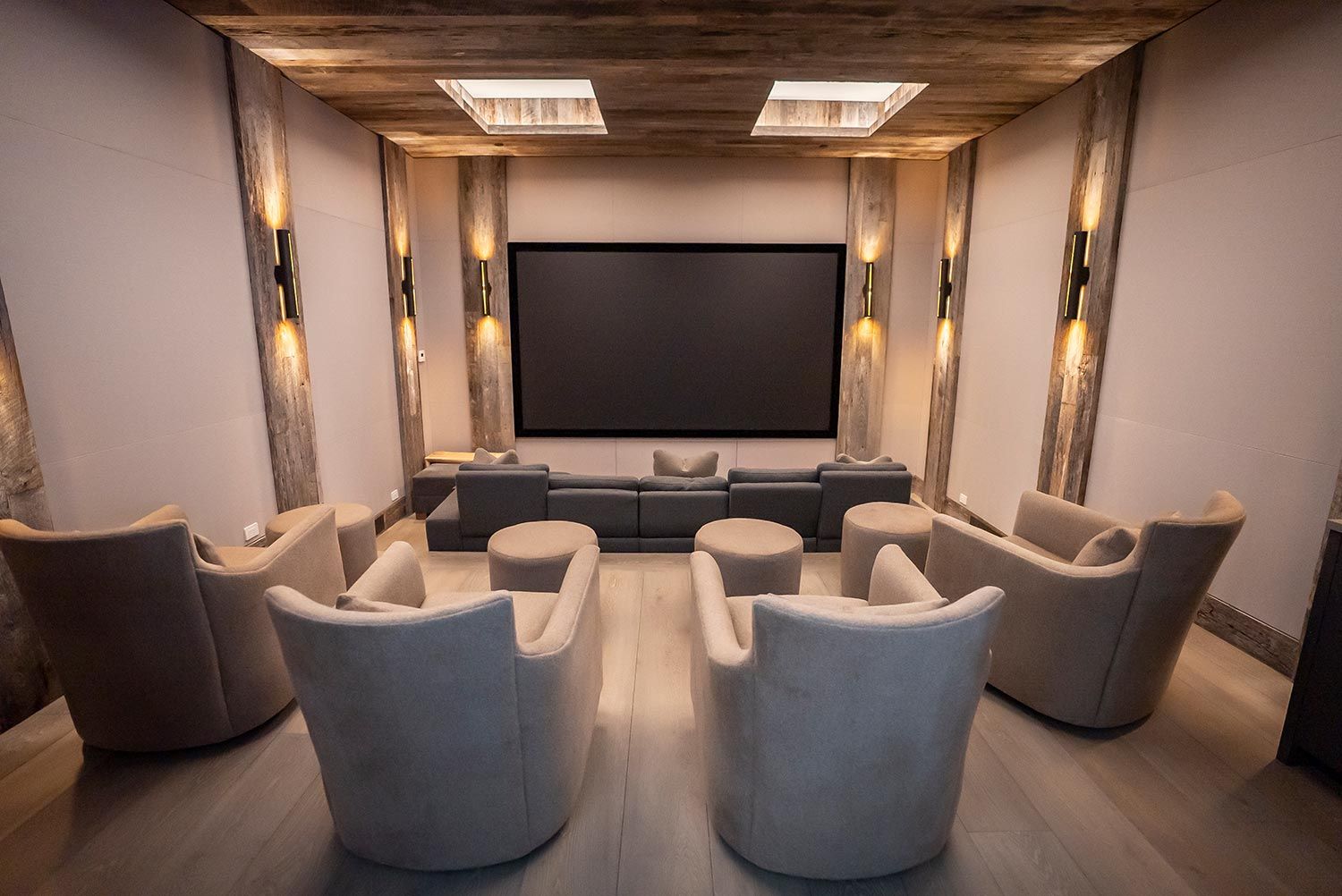 A rustic home theater with plush beige chairs, wooden beams, and soft lighting, creating a warm and intimate viewing experience.