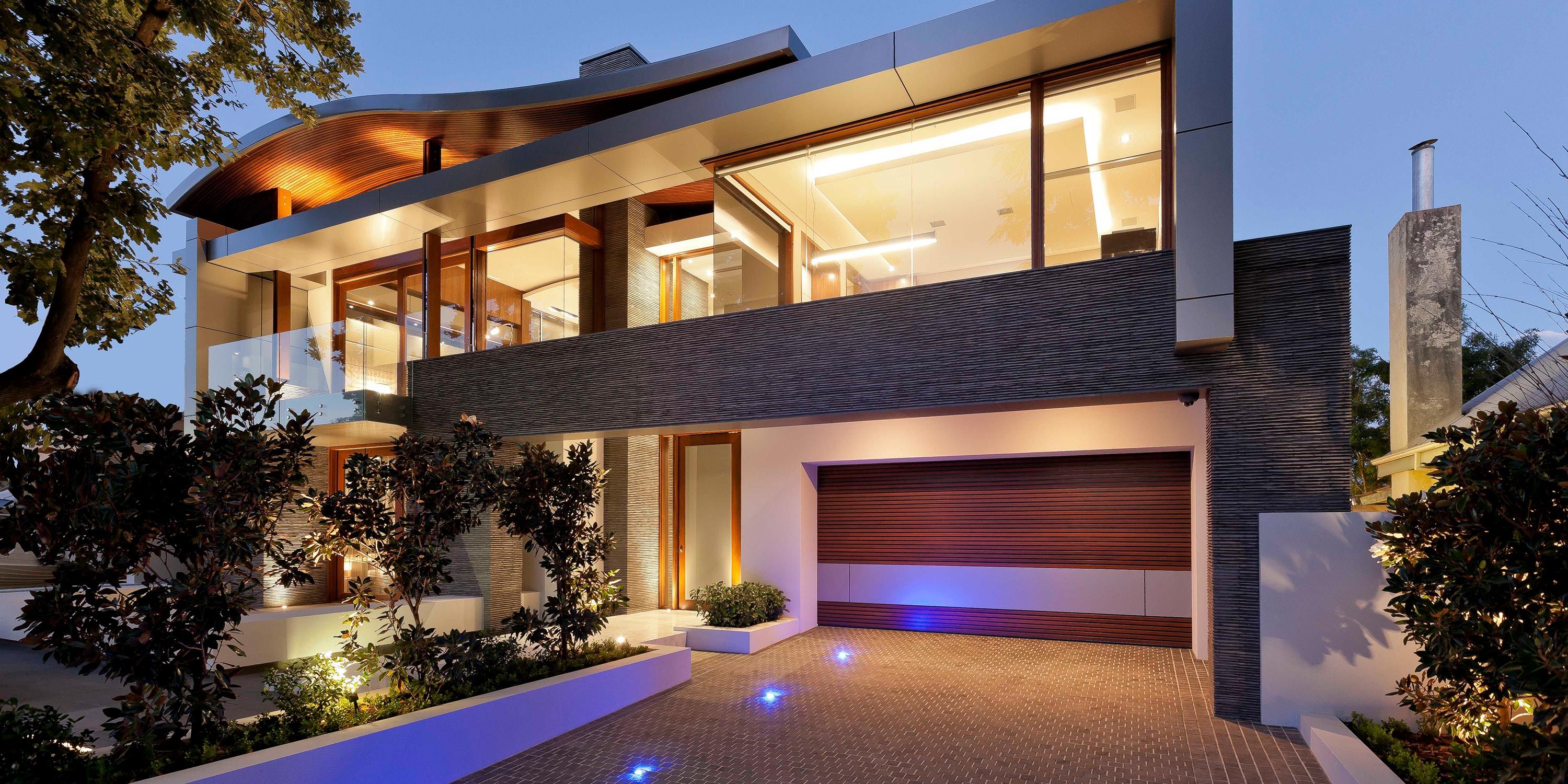 A well-lit modern home exterior with illuminated pathways and glass balconies.